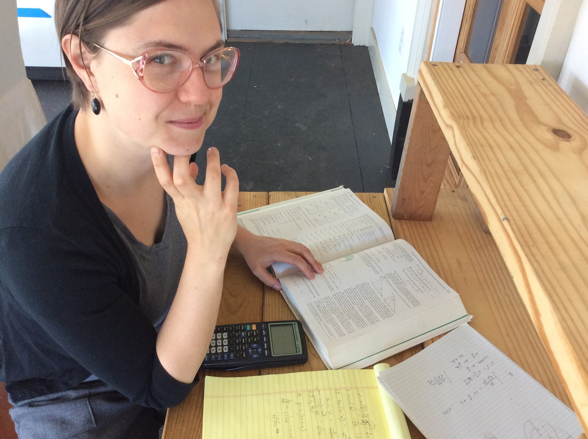 Miranda at her desk with a math textbook, graphing calculator, and worked problems on a yellow notepad